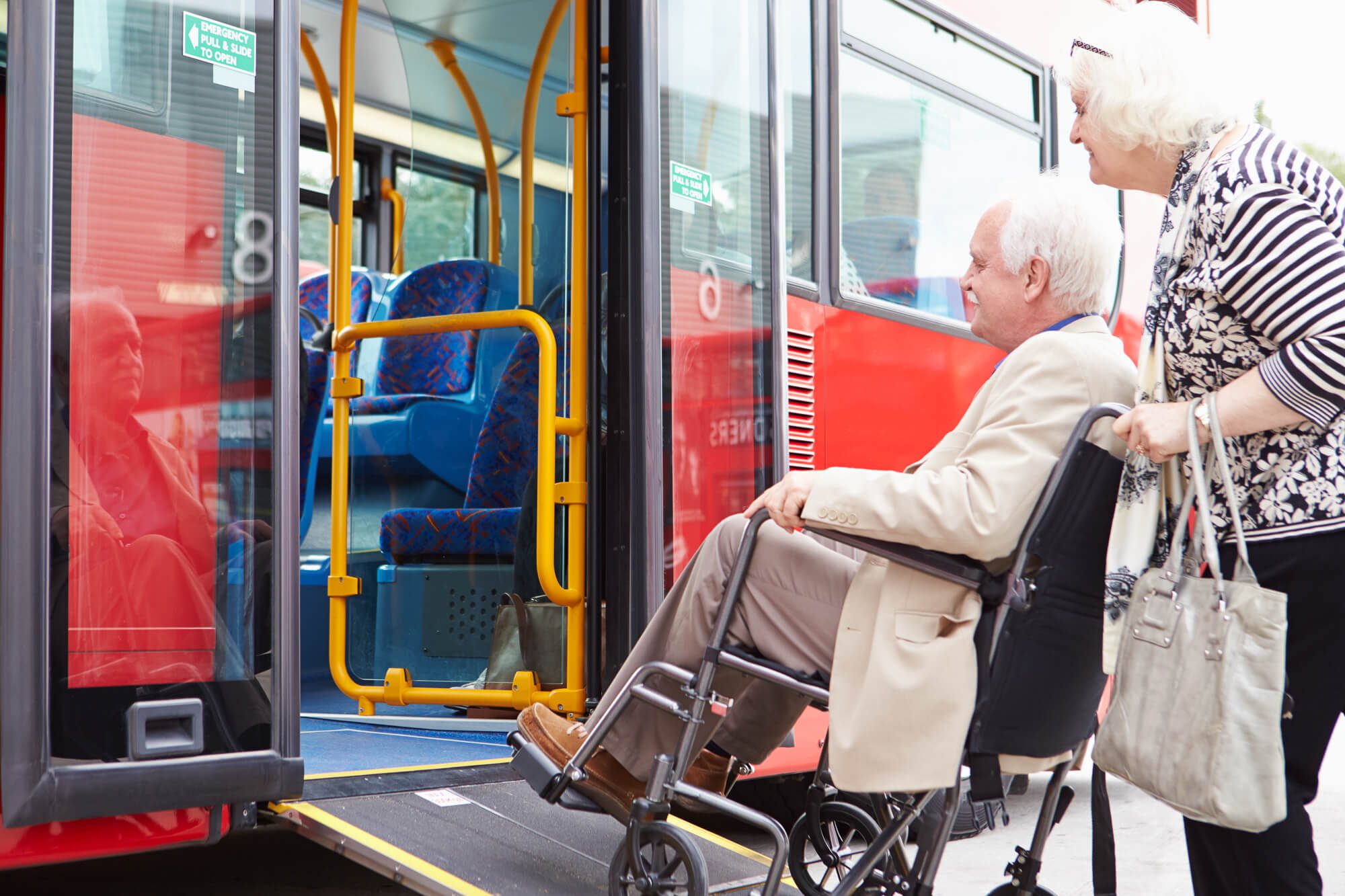 Woman pushing man in wheelchair boarding bus